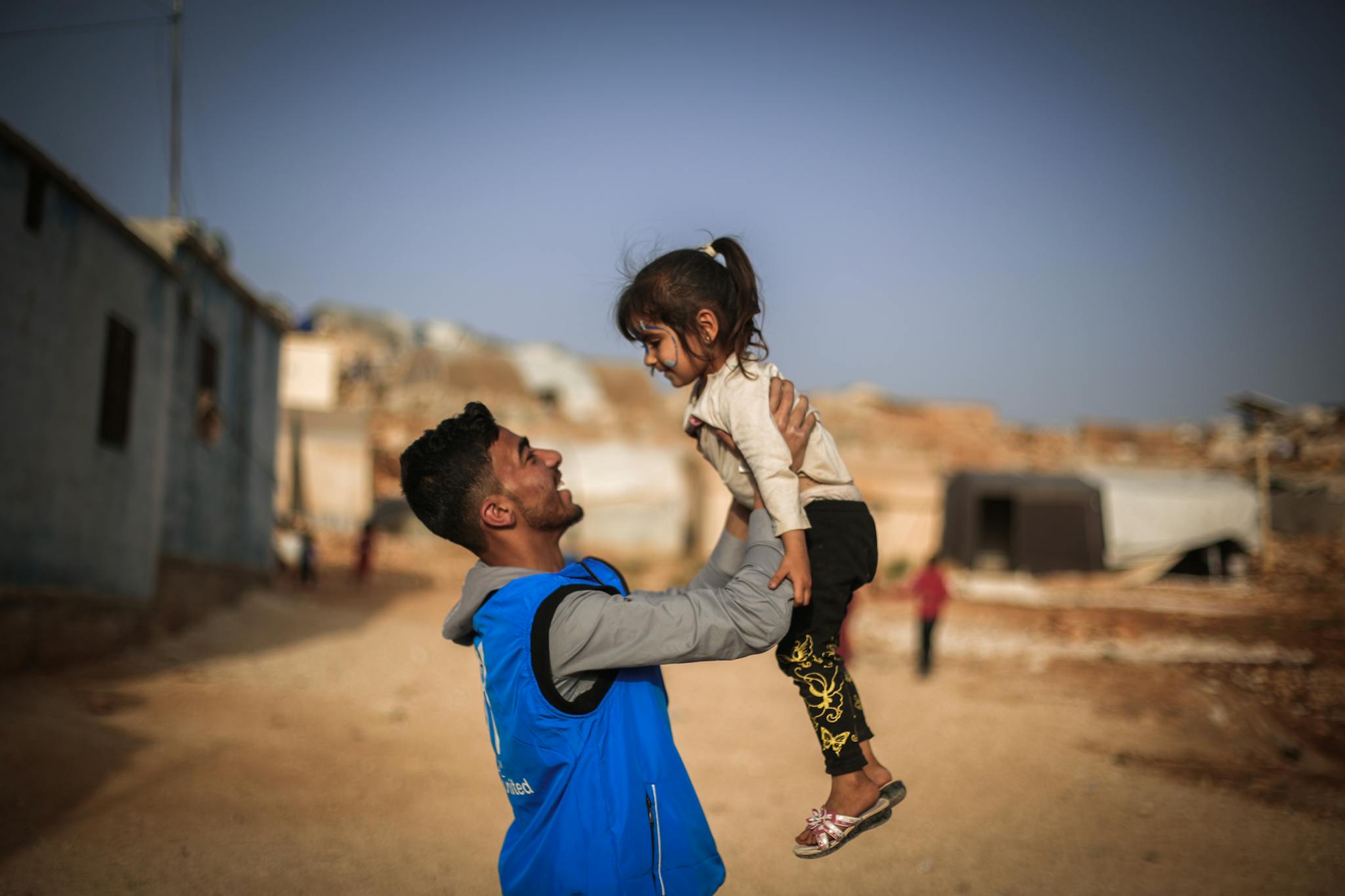 A touching moment of a father lifting his daughter in Idlib, capturing joy and connection.