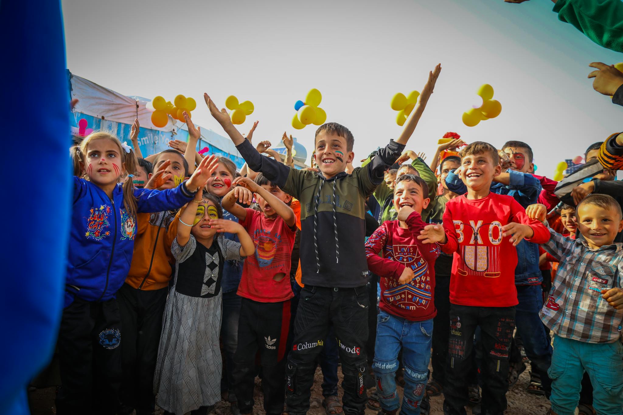 A vibrant group of children celebrate together outdoors in Idlib, Syria.