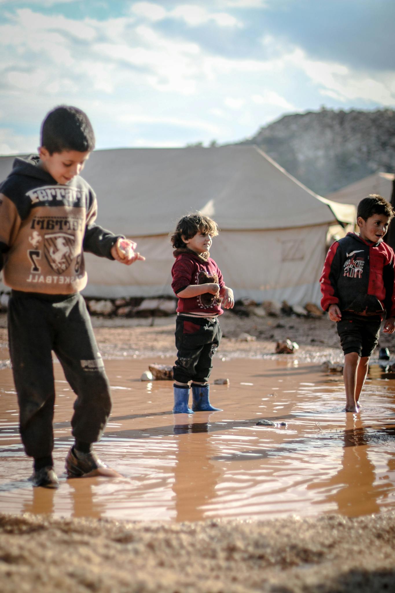 Children enjoying playtime in a muddy puddle at a refugee camp in Idlib, Syria.