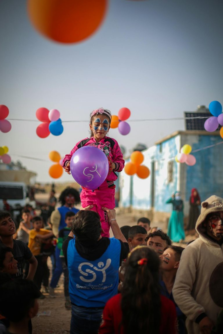 Vibrant festival scene with children playing and balloons in Idlib, Syria, showcasing joy and community.